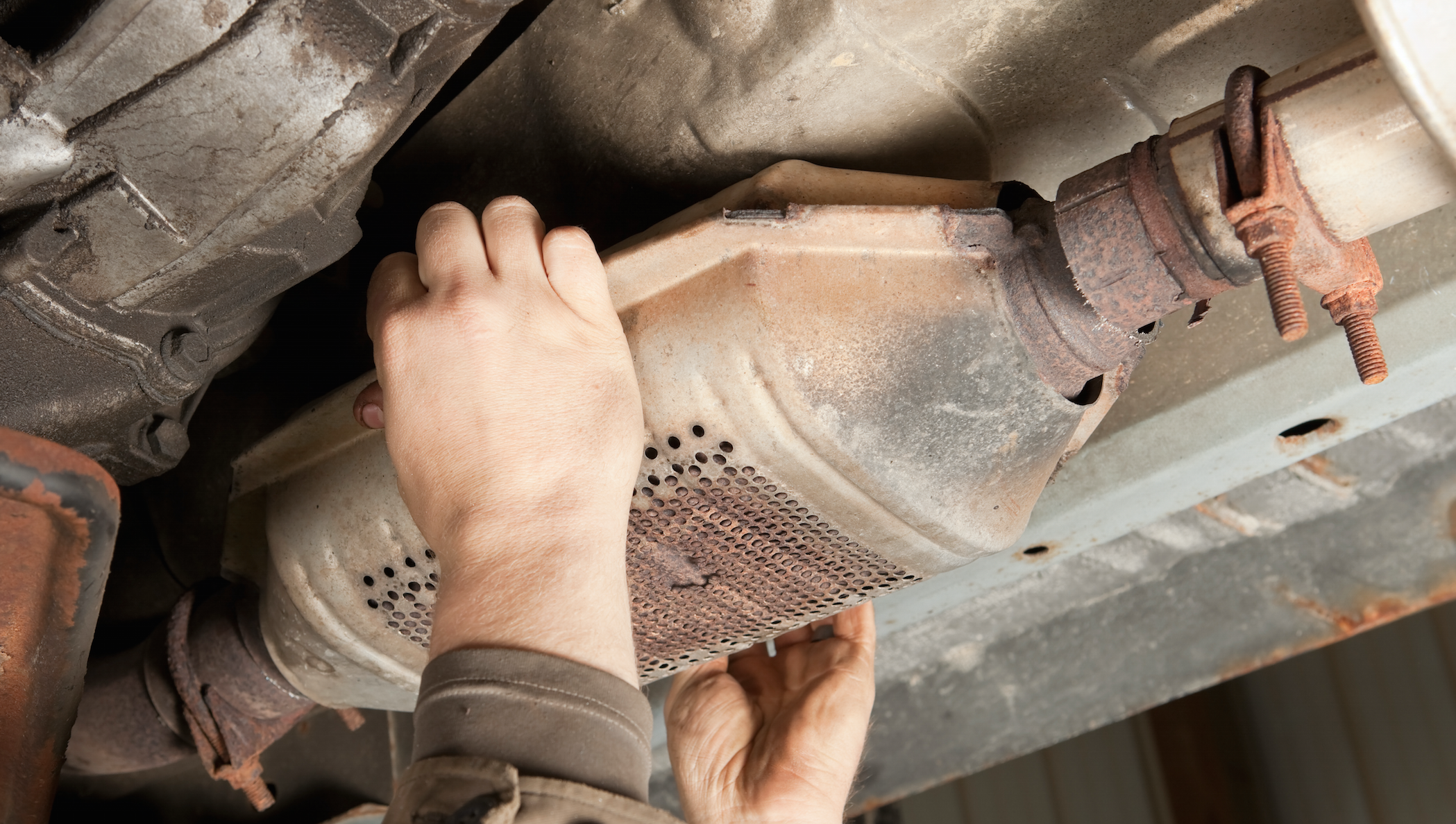 Person removing a catalytic converter from under a car