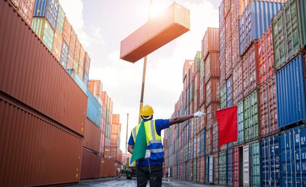 A worker at a container yard helping guide the placement of a cargo container lifted by a crane.