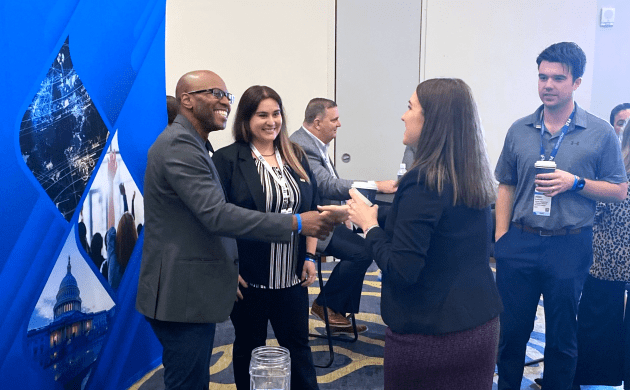 Several people in business dress smiling and shaking hands in a conference room.